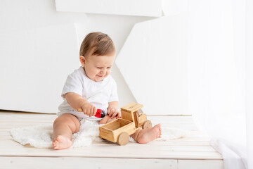 the kid is playing, happy cute little baby six months old in a white t-shirt and diapers sits on a light background at home and plays with a wooden typewriter, space for text