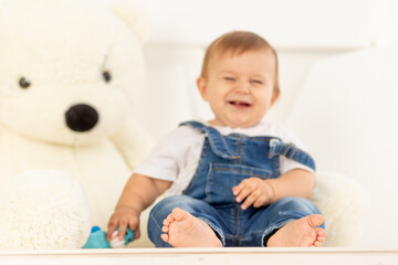 legs in focus, happy little baby six months old in blue jeans sits next to a large Teddy bear