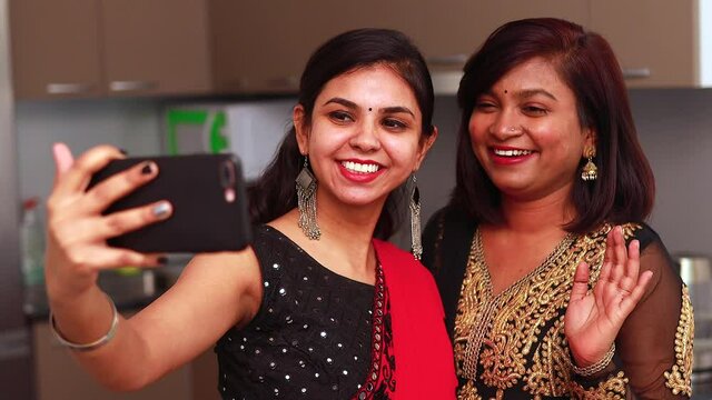 Two beautiful Indian woman talking with family online video call wearing ethnic traditional clothes for Diwali or another festival celebration