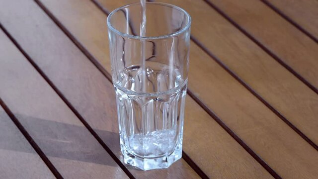Glass on a wooden table fills with water
