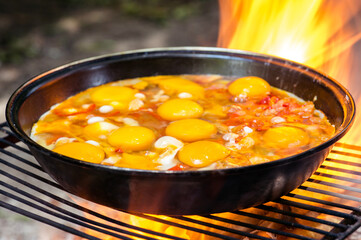 Fried eggs with vegetables in a frying pan on the grill close-up in the fiery flame of the fire. Background.