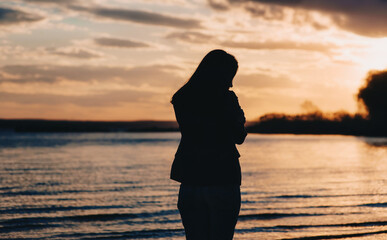 Silhouette of a young beautiful girl in jeans and a jacket against the backdrop of a cloudy sunset...