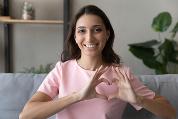 Close up portrait of smiling young indian Arabic woman show heart love hand gesture support sick....