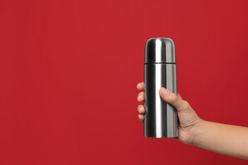 Woman holding modern thermos on red background, closeup. Space for text