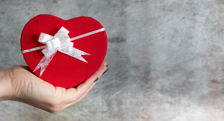 Mano sujetando caja de regalo roja en forma de corazón con lazo blanco