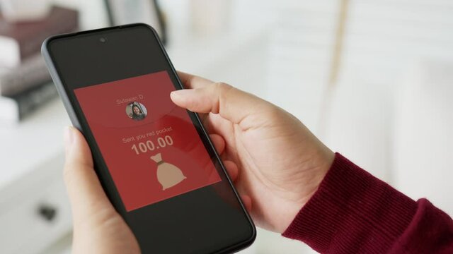 Asian female holding smartphone receiving lucky money or Ang Bao red pocket online via smart mobile banking application in lunar chinese new year traditional during quarantine contactless concept.