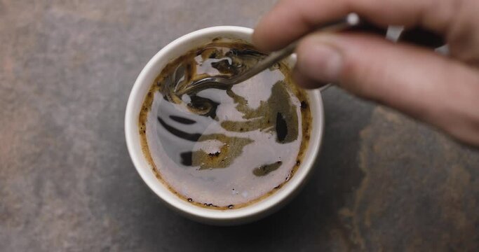 Hand stirring with a spoon of coffee in a white cup, slow motion. Blackmagic Ursa Pro G2. 