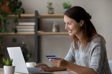 Overjoyed young woman buyer shopping online on laptop at home use credit card for payment. Smiling millennial female client make purchase buy on internet on computer. Secure banking system concept.