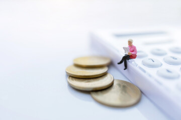 Miniature people: Businessman reading a book with coins and sitting on the calculator and calendar. Education or business concept.
