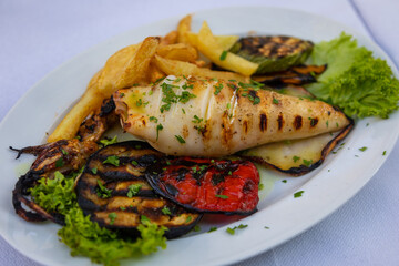 Grilled fresh squid on white plate with chips and vegetables.