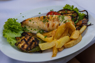 Grilled fresh squid on white plate with chips and vegetables.