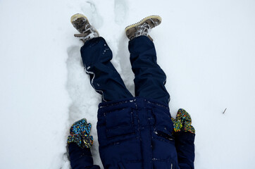 school boy in winter clothes playing in the snow. sometimes he lies on the ground on his back and...