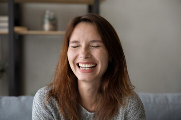 Close up of overjoyed millennial red-haired Caucasian woman feel glad joyful laugh relax at home. Happy young European female have fun joke and smile resting in living room. Happiness concept.