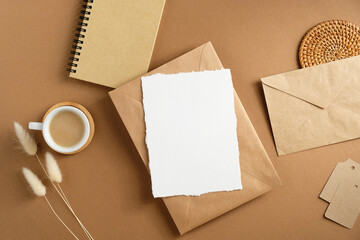 Blank paper card and envelope mockup on brown table with cup of coffee, notepad, dried flowers....