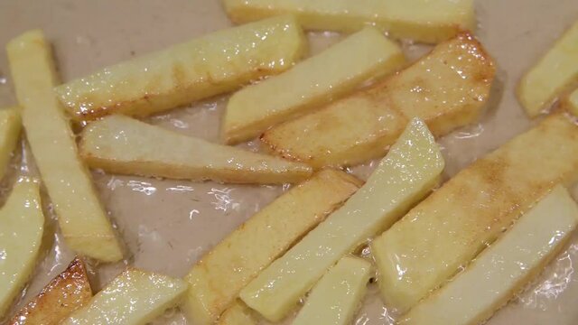 Close up of frying potatoes in hot boiling oil. Homemade french fries, fried in oil in a pan, the camera passes by the potato