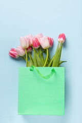 Fresh pink tulips in green paper bag on blue. Top view. Mothers day. Concept flowers delivery.