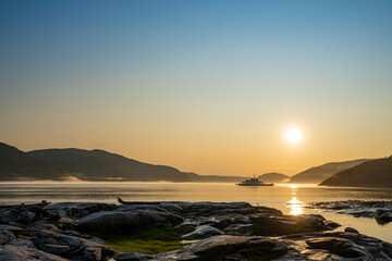 Ferry passing across Saguenay river in Tadoussac during sunset with a nice fog in background and birds in foreground