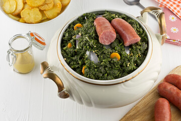 Kale in a soup tureen with sliced sausage and fried potatoes