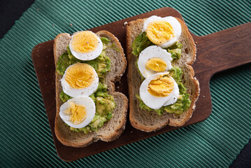 Sandwich prepared with oat toast, avocado and boiled egg, with dark backgrounds.