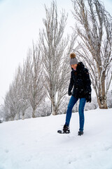 Chica joven en un parque nevado en un día de invierno con gorro de lana gris, jeans y cazadora negra