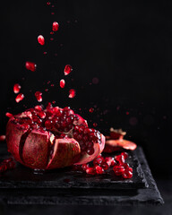 Freeze motion of sliced pomegranate red fruit with splashing juice, drops and seeds on black...