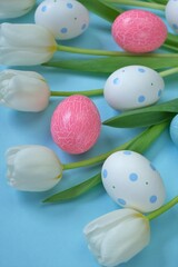 Fototapeta na wymiar Easter holiday. White tulips flowers, pink and spotted Easter eggs on a light blue background.. Easter eggs in pastel colors set.Spring festive easter background.Easter symbol.