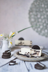 Unbaked creamy cheesecake with chocolate cookies and white cream biscuits on wooden table with flowers. Selective focus on desert cake with copy space.