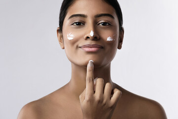 Beautiful Indian woman applying moisturizing cream on her face