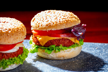 Tasty vegetarian food, homemade cheeseburgers made from plant based soya meat with cheese, onion, green lettuce and tomatoes