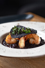 Black rice risotto. Shrimp risotto on a white plate on the table, serving in a restaurant, menu food concept