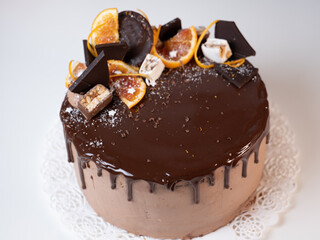 Fototapety  beautiful chocolate cake with oranges, drizzled with chocolate icing on a light table