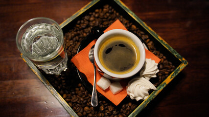 Close up of beautiful serve of cup of coffee and glass of water in stand with coffee beans. Top view of mug of hot drink with sugar and souffle in cafe.