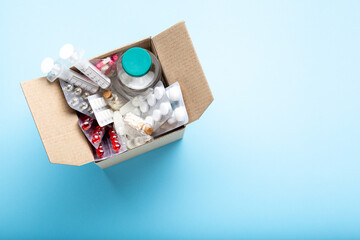 Delivery of medicines home from the pharmacy. Cardboard box with medicines, pills, bottles, injections isolated on blue background top view