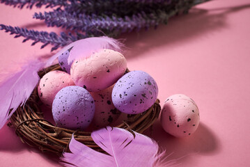 Obraz na płótnie Canvas Close Up of Colorful Easter Eggs with pastel colored feathers in the nest with lavender bouquet on the pink background. Pastel colors
