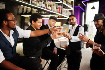 Cheers! Group of handsome retro well-dressed man gangsters spend time at club. Drinking whiskey at bar counter. Multiethnic male bachelor mafia party in restaurant.