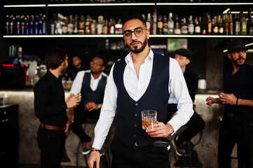 Stylish arab man against group of handsome retro well-dressed guys gangsters spend time at club, drinking on bar counter. Multiethnic male bachelor mafia party in restaurant.