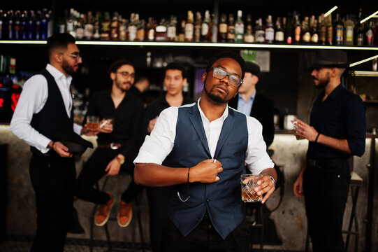 Stylish african american man against group of handsome retro well-dressed guys gangsters spend time at club, drinking on bar counter. Multiethnic male bachelor mafia party in restaurant.