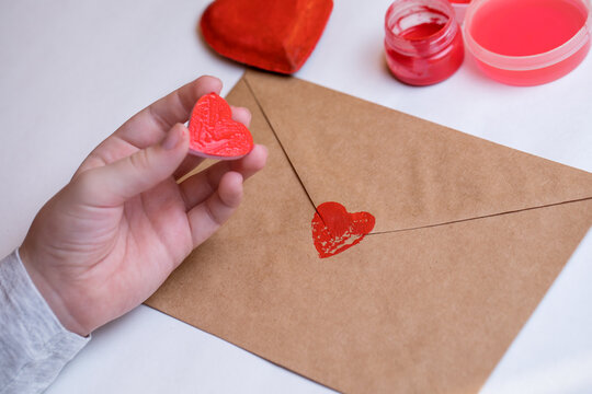 The child painted a wooden heart with red paint and made a print on the envelope. Preparing for Valentine's Day.