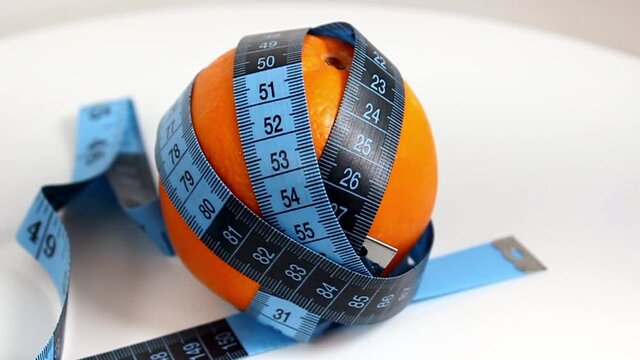 A ripe orange is wrapped in a blue centimeter ribbon. The concept of healthy eating and weight loss. Close-up.