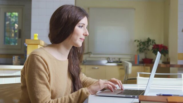 Freelance Happy young woman typing on computer laptop smiling with joy expression, sitting in modern interior kitchen table with agenda. Businesswoman success icon - Vertical frame