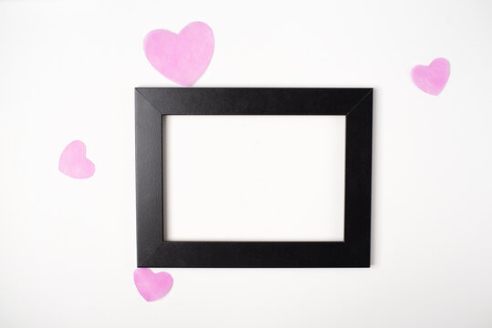 Black photo frame with pink hearts on the white background. Valentine's Day concept. Flat lay, top view, space for text.