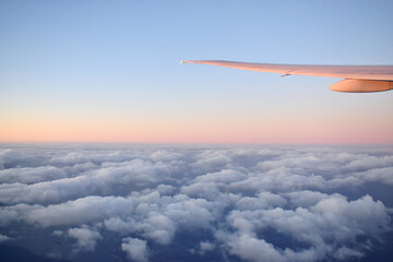 Fototapeta na wymiar Aircraft wing above cloudscraper with horizon of pink and blue sky,view from airplane window.