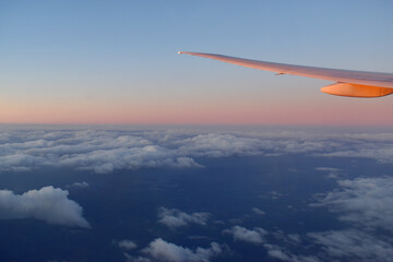 Aircraft wing above cloudscraper with horizon of pink and blue sky,view from airplane window.