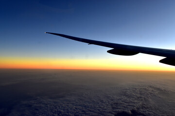Silhouette of Airplan wing in twilight sky, with beautiful light from dramatic sunset, Romantic view from airplane window.