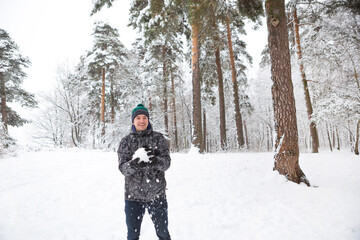 Fototapeta na wymiar A young man with a snowball in his hand is having fun, swinging for a throw. Winter family and friendly games and entertainment in the forest with snow in the open air
