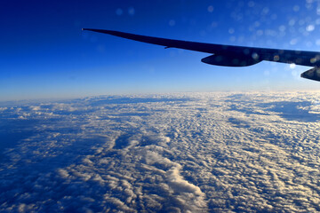 Beautiful clouds on the sky with dramatic light and blue sky background under Aircraft wing, view from airplane window.