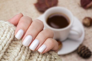 Beautiful hand of a young woman with a knitted sweater and autumn leaves. The nails are covered with a white gel Polish with a shimmer. Manicure ideas.