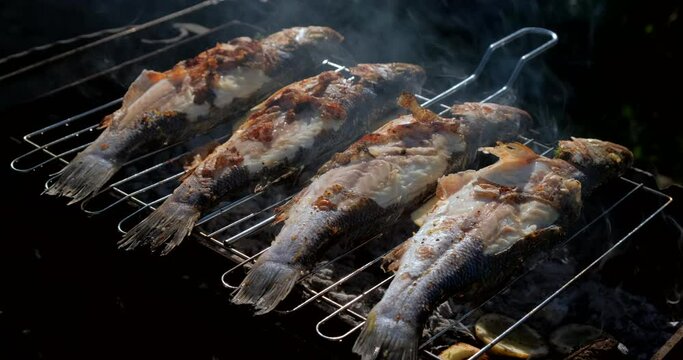 Sea bass or grouper fish grilled over charcoal. Close-up shot cooking seafish with aromatic spices on barbecue grill plate. Baking roasting marinated delicious seafood. BBQ  in summer garden outdoors 