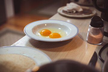 Two raw eggs cracked in white plate. Food preparing in domestic kitchen.