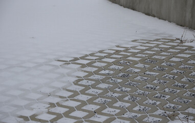 grass gray concrete tiles snowed only in part. The paving is filled with gravel. serves as a...
